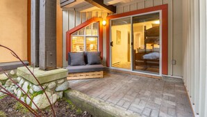 A cozy outdoor seating area with a stone bench, a wooden table, and a cushioned bench with pillows.