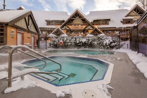 Ein Poolbereich mit verschneitem Deck, einem Rettungsschwimmerstuhl und einem Gebäude mit Holzfassade und Schnee auf dem Dach.