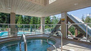 An indoor swimming pool with a wooden deck, glass railings, and a view of a forested area. - Mountainside 2Br/2Ba - Hot Tub/Pool/Free Parking (Whistler)