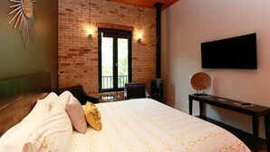 Une chambre avec un mur en briques, un lit avec une literie à motifs, une télévision et un objet décoratif rond posé sur une table.