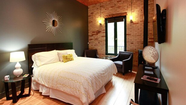 Une chambre à coucher avec un lit, une table de chevet, une lampe, une chaise, un piano et une fenêtre.