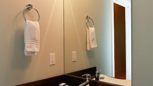 Une salle de bain avec un lavabo blanc, un miroir et deux serviettes suspendues à des porte-serviettes.