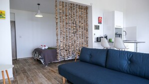 Ein modernes Wohnzimmer mit einem blauen Sofa, einem Esstisch mit Stühlen, einer Küchenzeile und einer Wand mit dekorativen Accessoires.