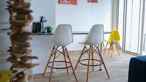 Ein modernes Interieur mit zwei weißen Stühlen mit Holzbeinen, einem gelben Stuhl und einer Küchenzeile mit einer Kaffeemaschine.