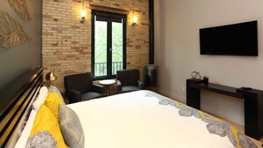 A bedroom with a brick wall, a bed, two chairs, a small table, a TV, and a fireplace. - Discover the cozy Napoli Suite in the heart of downtown Saugatuck, a charming retreat for two. (Saugatuck)