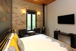 A bedroom with a brick wall, a bed, two chairs, a small table, a TV, and a fireplace.