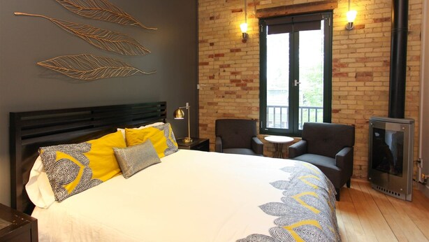 A bedroom with a bed, two chairs, a small table, a fireplace, and a window with a view. - Discover the cozy Napoli Suite in the heart of downtown Saugatuck, a charming retreat for two. (Saugatuck)