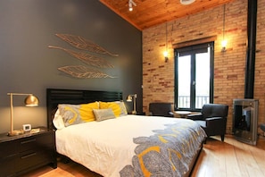 A bedroom with a bed, a nightstand, a lamp, a chair, a table, and a fireplace.
