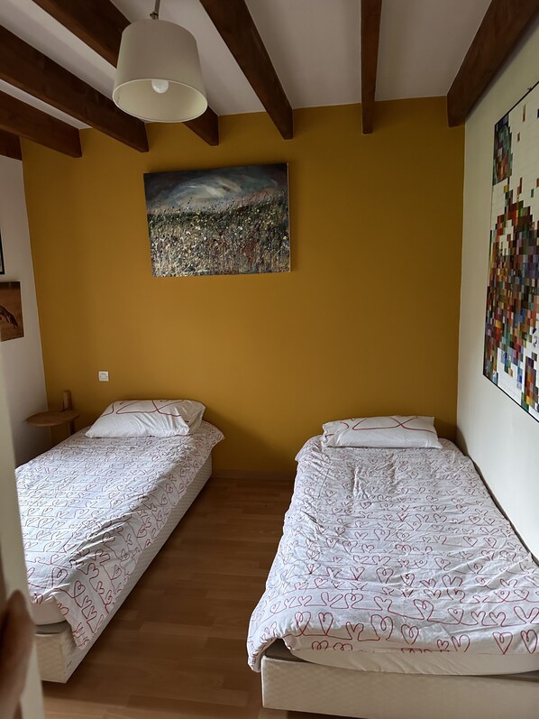 Una habitación con dos camas, vigas de madera, una lámpara en el techo, un cuadro y un colcha en la pared.