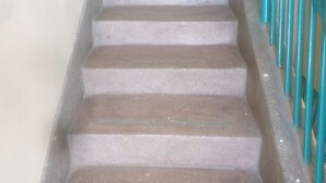 Un escalier avec des marches en béton et une rampe métallique turquoise.