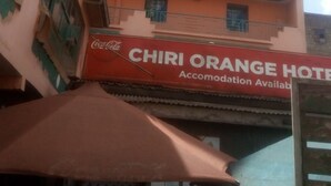 Un immeuble à plusieurs étages doté de balcons et d’une enseigne Coca-Cola. L’immeuble porte une enseigne indiquant « HÔTEL CHIRI ORANGE » et « TOWERS ».