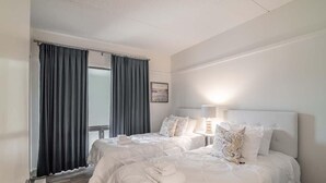 A hotel room with two beds, a window with curtains, a bedside table with a lamp, and a framed picture on the wall. - Litchfield Retreat near Brookgreen Gardens (Pawleys Island)