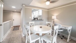 A dining area with a round table and white chairs, a ceiling fan, and a kitchen visible through an open door. - Litchfield Retreat near Brookgreen Gardens (Pawleys Island)
