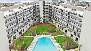 A multi-story hotel with a central swimming pool surrounded by lounge chairs and palm trees. - Litchfield Retreat near Brookgreen Gardens (Pawleys Island)