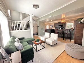 A spacious living area with a green sofa, white armchairs, a coffee table, and a kitchen in the background. - Welcome to Dacha! Long term winter rental now available! (Spring Lake)