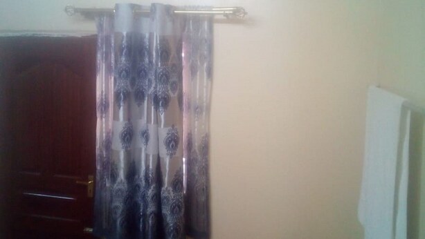 A room with a door, a curtain, a small table, and a trash bin. - Desai Annex Guest House (Nairobi)