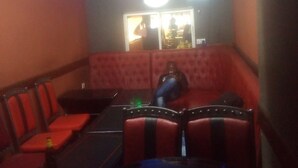 A dimly lit room with red upholstered seating and a table. A sign on the wall reads "NO IDLE SITTING." - Desai Annex Guest House (Nairobi)
