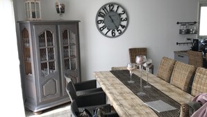 Een eethoek met een lange tafel, rieten stoelen en een grote wandklok.