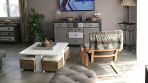 Een moderne woonkamer met een groot flatscreen televisietoestel aan de muur, een bank, een salontafel en een houten stoel.