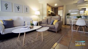 A modern living room with a sofa, two coffee tables, and a dining area with a chair. - Apartamento del Cabo I (Ventorros de San José)