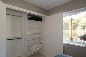 A room with a built-in closet, a window with a view of a body of water, and a bed.