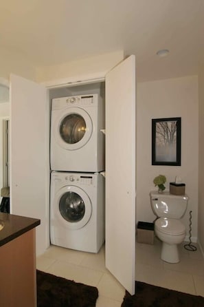 A compact laundry room with two stacked washing machines and a toilet.