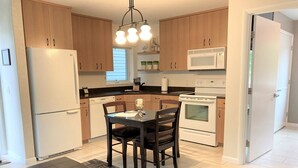 Une cuisine moderne avec des meubles en bois, un réfrigérateur blanc, un four à micro-ondes et une cuisinière. On y trouve une table à manger avec des chaises et un tapis sur le sol.