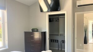 A bedroom with a bed, a dresser, a TV, an air conditioner, and a closet.