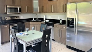 A modern kitchen with stainless steel appliances, wooden cabinets, and a glass dining table.
