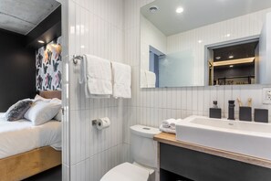 Een moderne badkamer met een groot wastafel, toilet en douche. Handdoeken hangen aan een rek en er is een spiegel boven de wastafel.