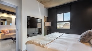A modern hotel room with a large bed, a TV mounted on the wall, a sofa in the adjacent living area, and a window with a city view. - Eclectic Loft with All Amenities (Montréal)