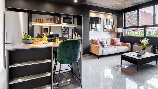 A modern kitchen with a built-in oven and microwave, a dining area with a green chair, and a sofa with a view of the city. - Eclectic Loft with All Amenities (Montréal)