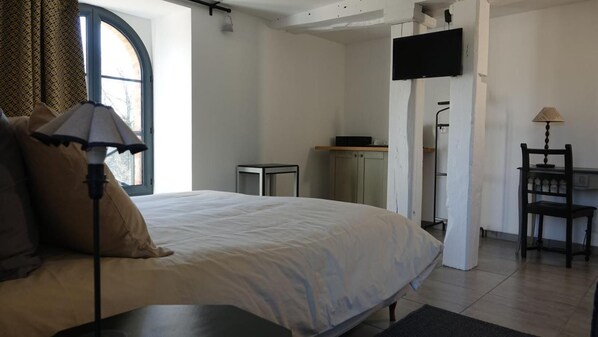 A bedroom with a large bed, a desk, a chair, a television, and a window with curtains. - L'Ilot du Moulin (Mordelles)