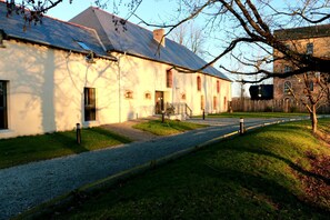 A building with a gravel path leading to the entrance, a wooden fence, and a tree in the foreground. - L'Ilot du Moulin (Mordelles)