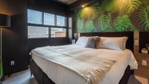 A modern hotel room with a large bed, a view of the city through large windows, and a tropical leaf-patterned wall. - Ambient Loft with All Amenities (Montréal)