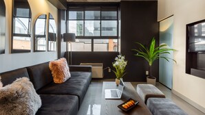 A modern living room with a black sofa, a coffee table with a laptop, a potted plant, and a large window with a view of buildings. - Ambient Loft with All Amenities (Montréal)