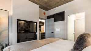 A modern hotel room with a large bed, a flat-screen TV mounted on the wall, a wardrobe, and a door leading to a bathroom.