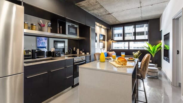 Une cuisine moderne dotée d’appareils électroménagers en acier inoxydable, d’un îlot central et offrant une vue sur la ville grâce à de grandes fenêtres.
