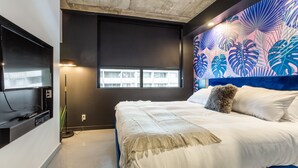 Une chambre moderne avec un grand lit, un téléviseur à écran plat et une fresque murale aux couleurs vives représentant un paysage tropical.