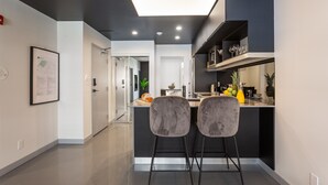 A modern kitchen with a central island, two bar stools, and a dining area with a white table and chairs. - Central Apartment with All Amenities (Montréal)