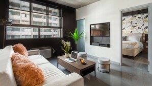 A modern living room with a sofa, a coffee table with a laptop, a potted plant, and a TV on the wall. - Central Apartment with All Amenities (Montréal)