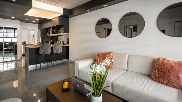 A modern living room with a sofa, coffee table, and a laptop. There is a kitchen area in the background with a dining table and chairs. - Central Apartment with All Amenities (Montréal)
