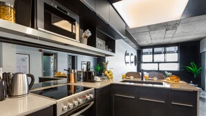 A modern kitchen with stainless steel appliances, a large island with a sink, and a view of the city through large windows. - Central Apartment with All Amenities (Montréal)