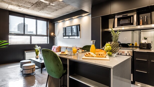 A modern kitchen with a central island, a dining area with a green chair, and a large window with a city view. - Modern Loft near McGill University (Montréal)