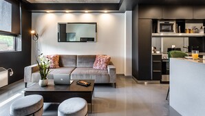 A modern living room with a grey sofa, a coffee table, and a laptop. There is a kitchen area with a microwave and a green chair. - Modern Loft near McGill University (Montréal)