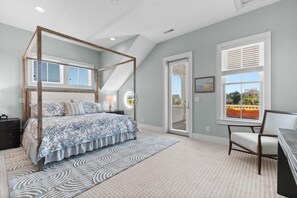 Ein Schlafzimmer mit einem Himmelbett, einem großen Fenster mit Jalousien, einem Sessel und Blick ins Freie.