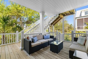 A covered outdoor deck with a sofa and coffee table, white railings, and a staircase.