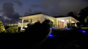 Een tweelaags huis met een balkon, een overdekte veranda en een oprit met blauwe verlichting.