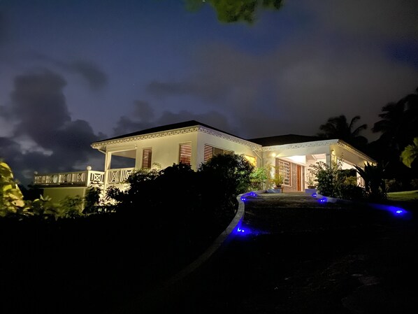 Une maison à deux étages dotée d’un balcon, d’un porche couvert et d’une allée éclairée de lumières bleues.