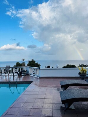 Un espace aménagé au bord de la piscine, offrant une vue sur l’océan et un arc-en-ciel.